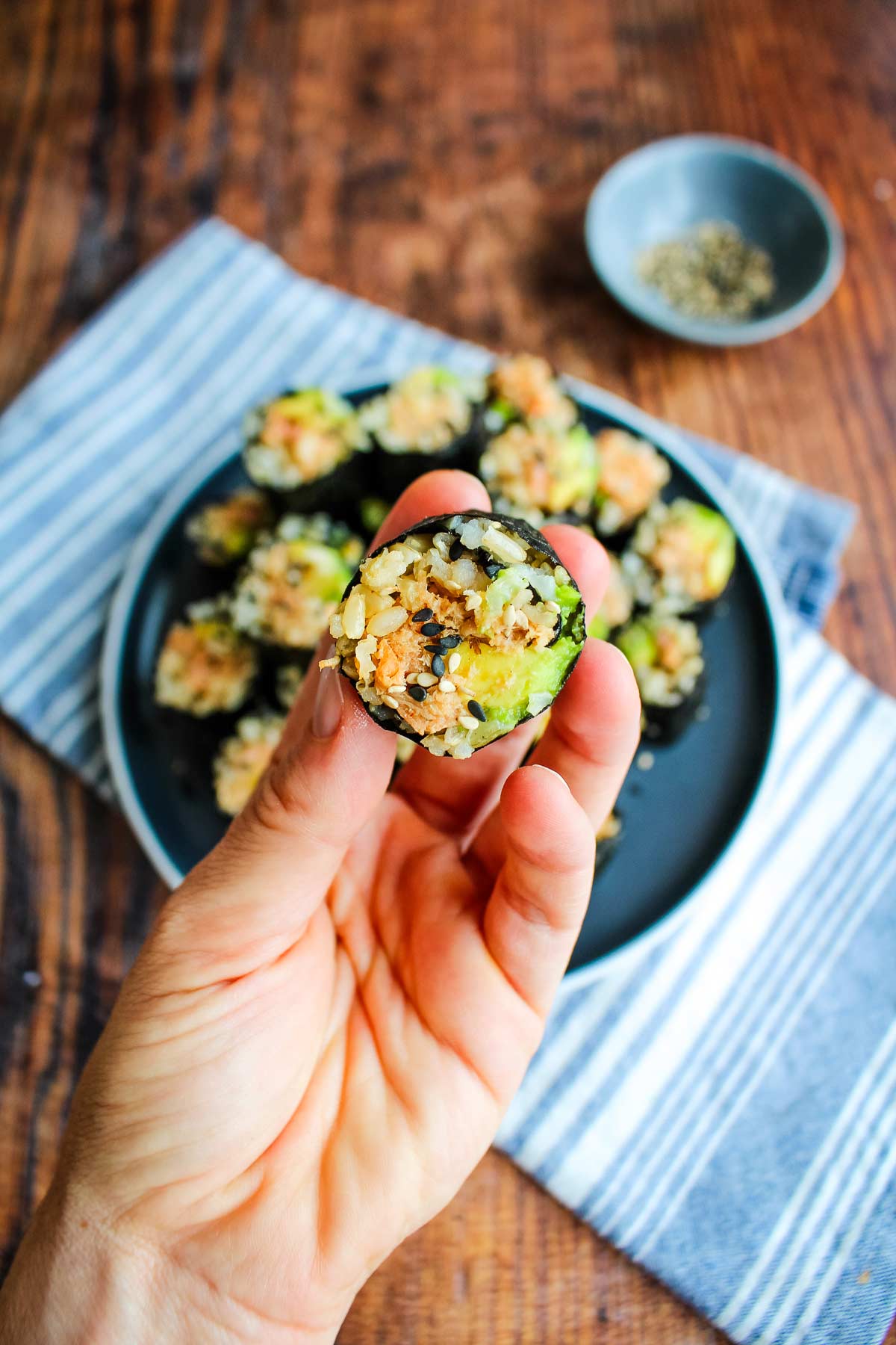 A hand holding up a piece of salmon onigiri roll up over the plate.