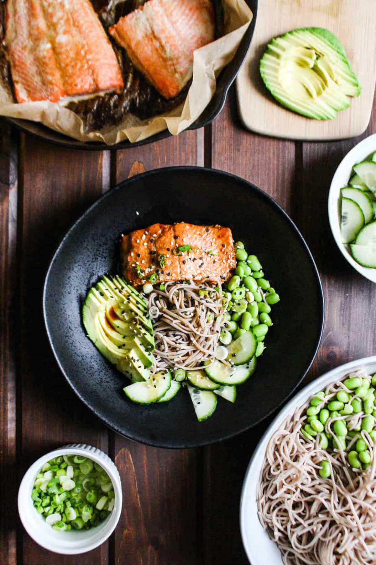 Salmon with soba noodles in a bowl with edamame, cucumbers, and avocado.