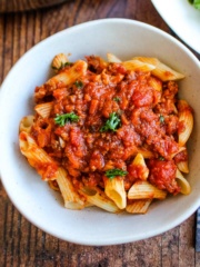 A bowl of pasta topped with sausage bolognese with mushrooms on the table.