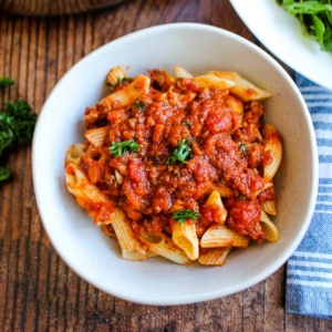 A bowl of pasta topped with sausage bolognese with mushrooms on the table.