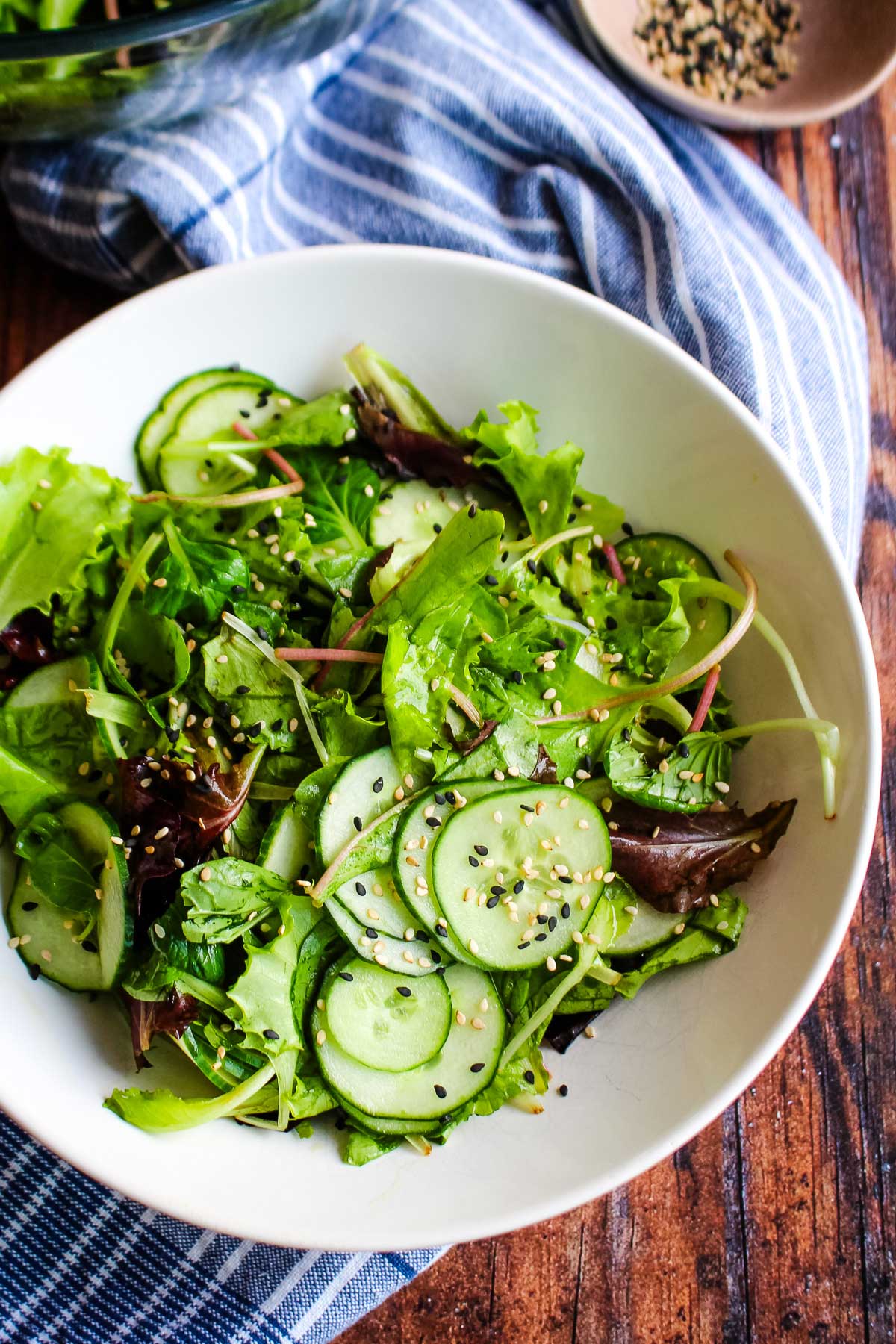 A bowl of Asian cucumber salad with sesame dressing on the table with a blue towel.