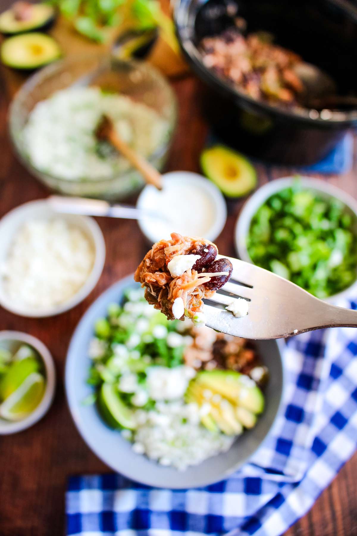 A bite of crockpot chicken burrito bowl held up over the bowl and the table.