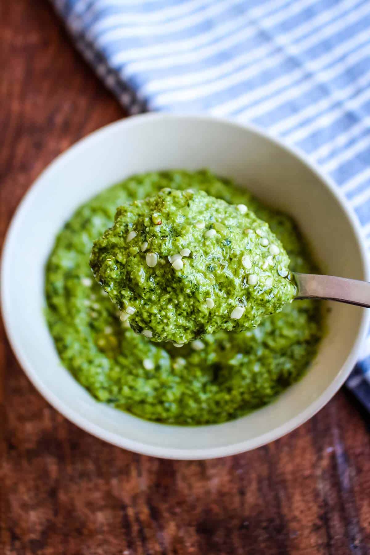A bowl of paleo pesto with spinach and basil on the table with a spoonful held above it.