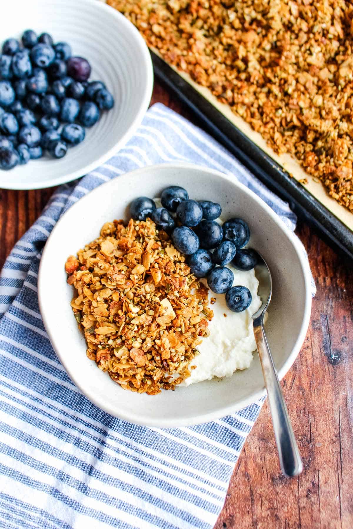 A bowl of high protein vanilla granola on the table with yogurt and berries.