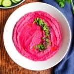 White bean hummus with beets in a bowl and garnished with fresh herbs.