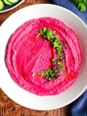 White bean hummus with beets in a bowl and garnished with fresh herbs.