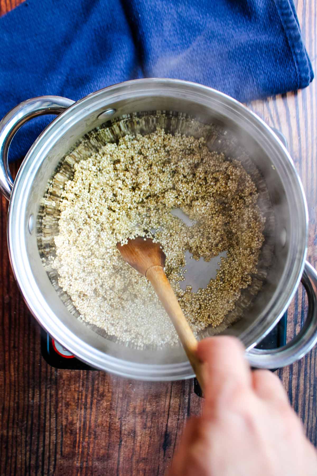 Toasting the quinoa in a pot with a hand stirring a wooden spoon.