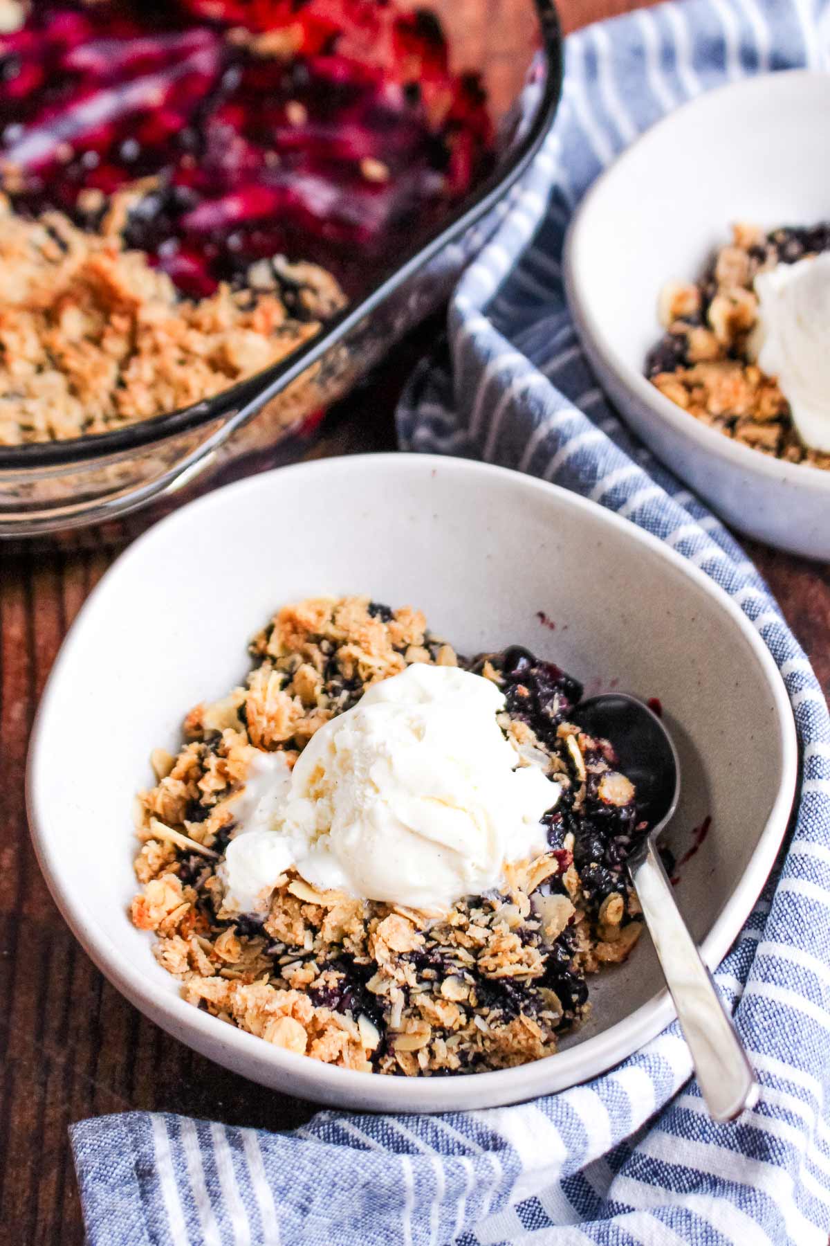 A bowl of gluten-free blueberry crisp topped with ice cream and a spoon in the bowl.