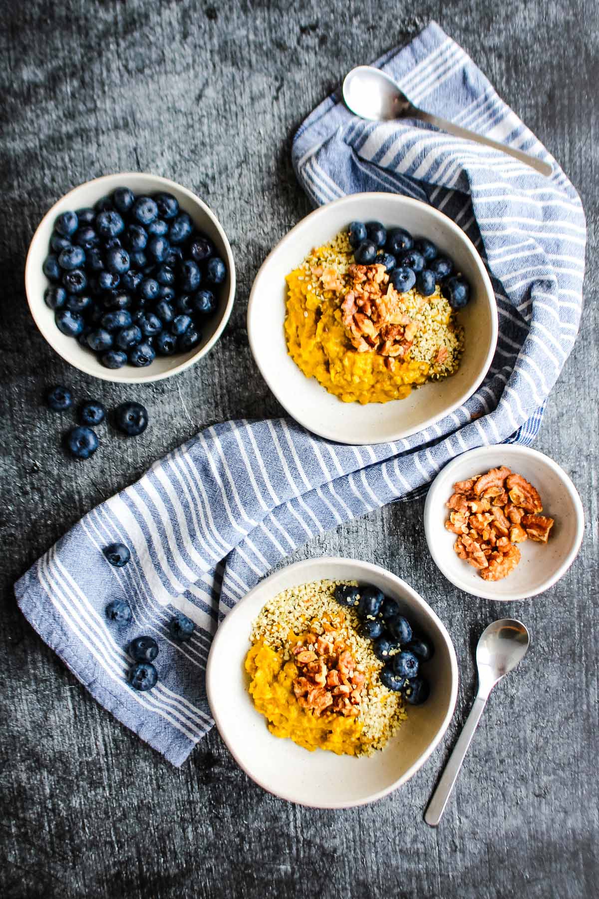 An overhead of two bowls of golden oats on the table with a bowl of blueberries.