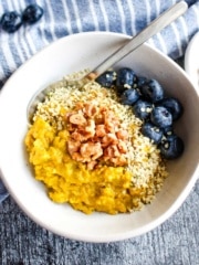 A bowl of golden milk oatmeal with a spoon and blueberries in the bowl.