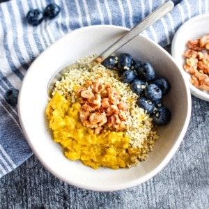 A bowl of golden milk oatmeal with a spoon and blueberries in the bowl.