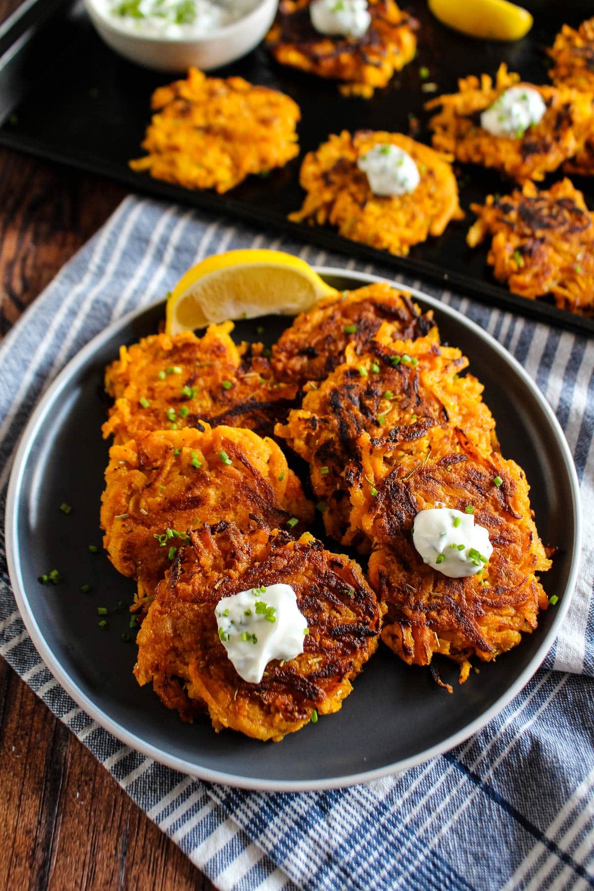 Butternut squash fritters on a plate with more on a pan in the background and topped with a creamy sauce.