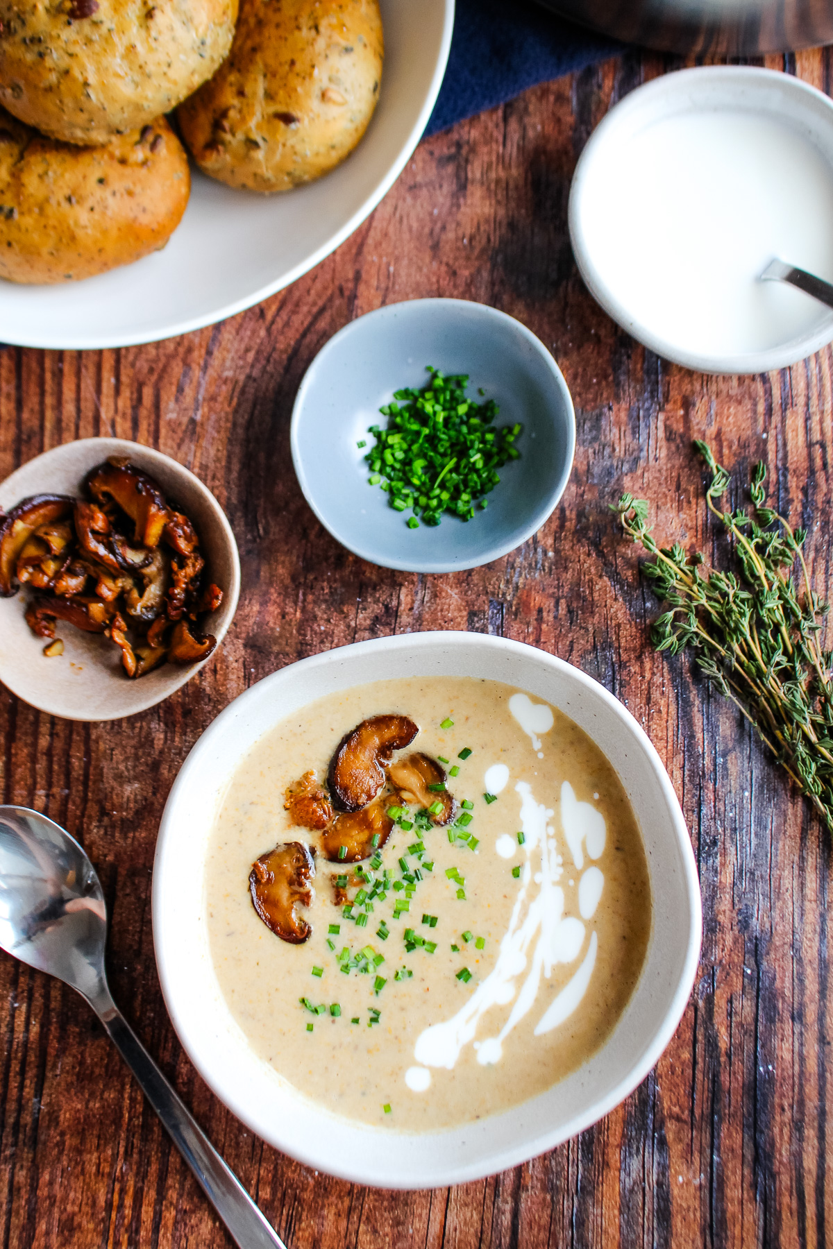 Mushroom bisque served up in a bowl on the table with some cooked mushrooms and chives in a small bowls.