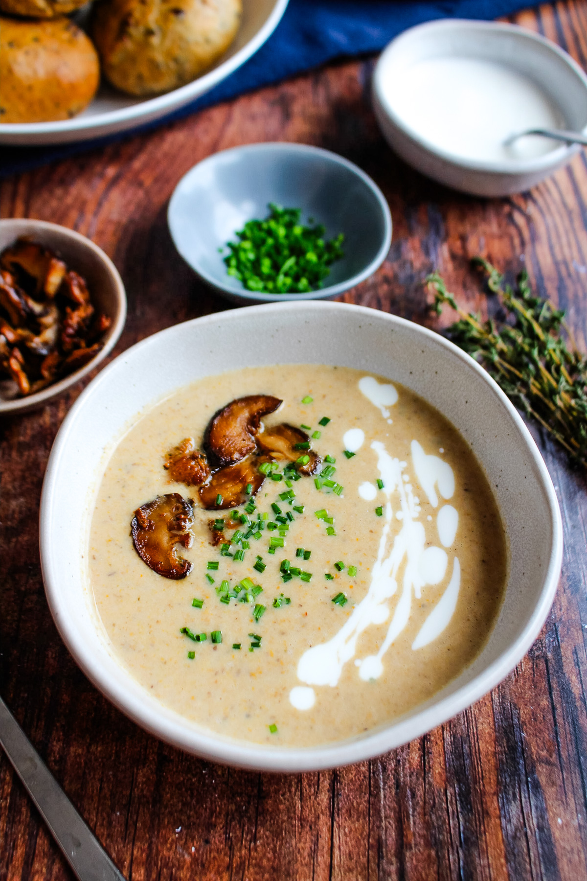 A bowl of mushroom bisque soup on the table topped with sour cream drizzle and mushrooms.