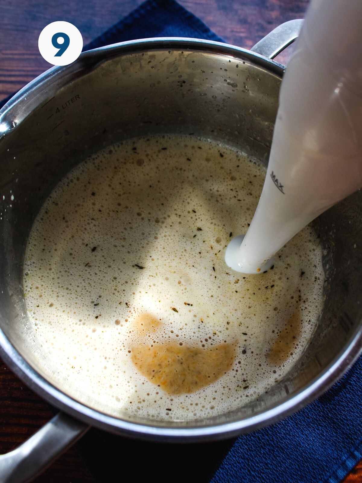 An immersion blender blending the soup in the pot.