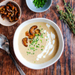 Bowl of mushroom bisque soup topped with browned mushrooms, chives, and some creamy drizzle.