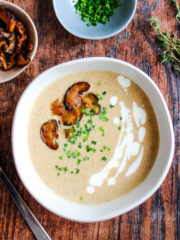 Bowl of mushroom bisque soup topped with browned mushrooms, chives, and some creamy drizzle.