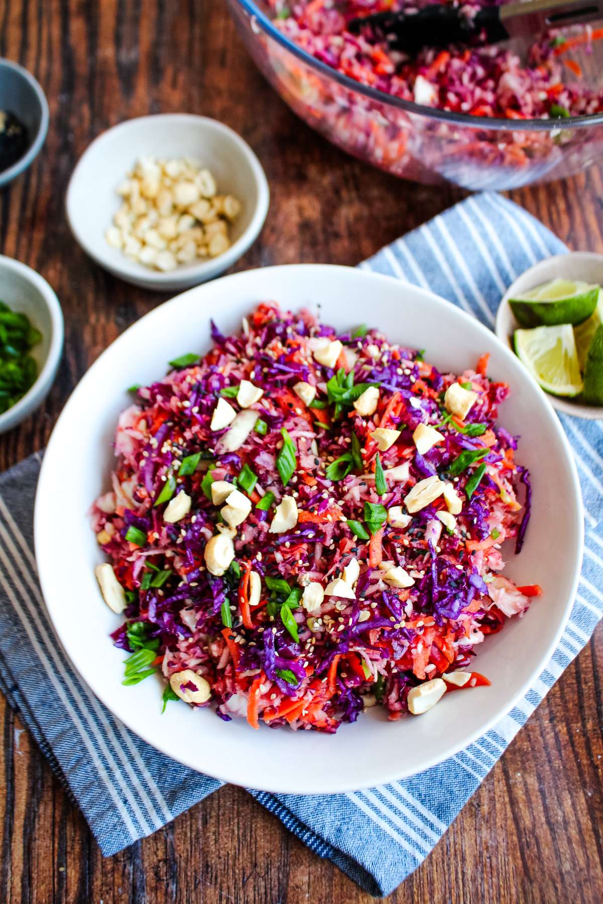 Cabbage crunch salad in a bowl on the table with small bowls of ingredients around the bowl.