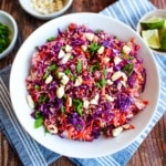 A bowl of cabbage crunch salad on the table surrounded by small bowls of ingredients.