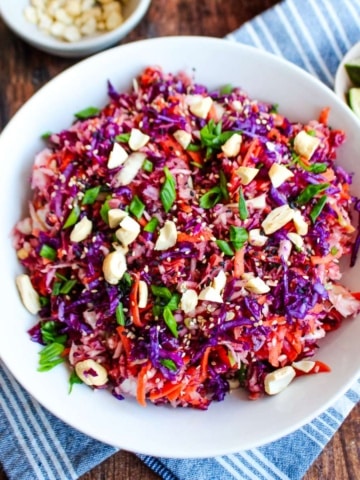 A bowl of cabbage crunch salad on the table surrounded by small bowls of ingredients.