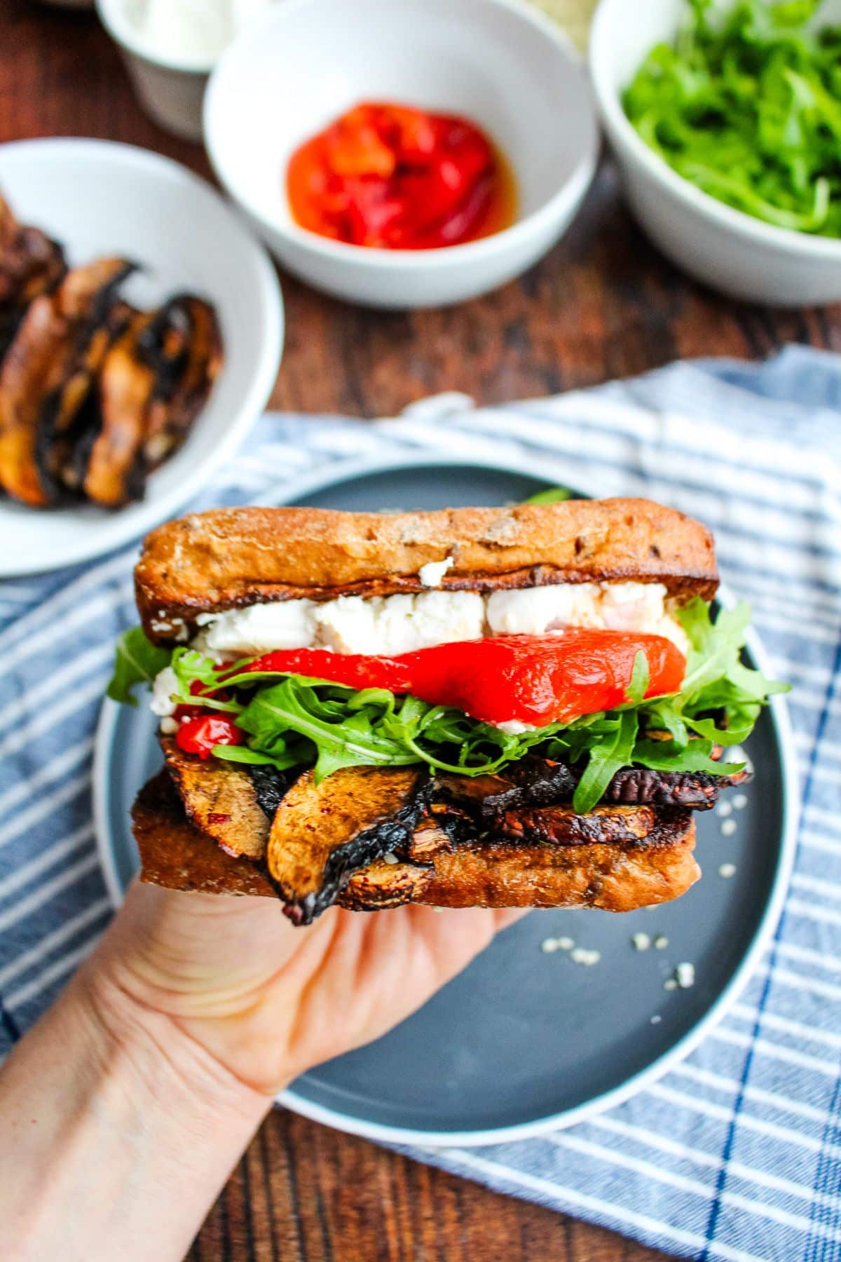 A hand holding up a portobello sandwich after it's made.