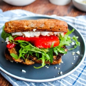 A portobello sandwich on a blue plate with lettuce tomato, and cheese peaking out.