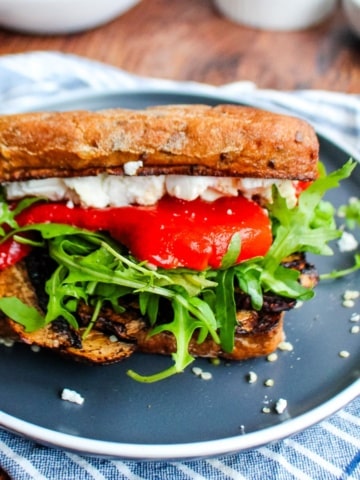 A portobello sandwich on a blue plate with lettuce tomato, and cheese peaking out.