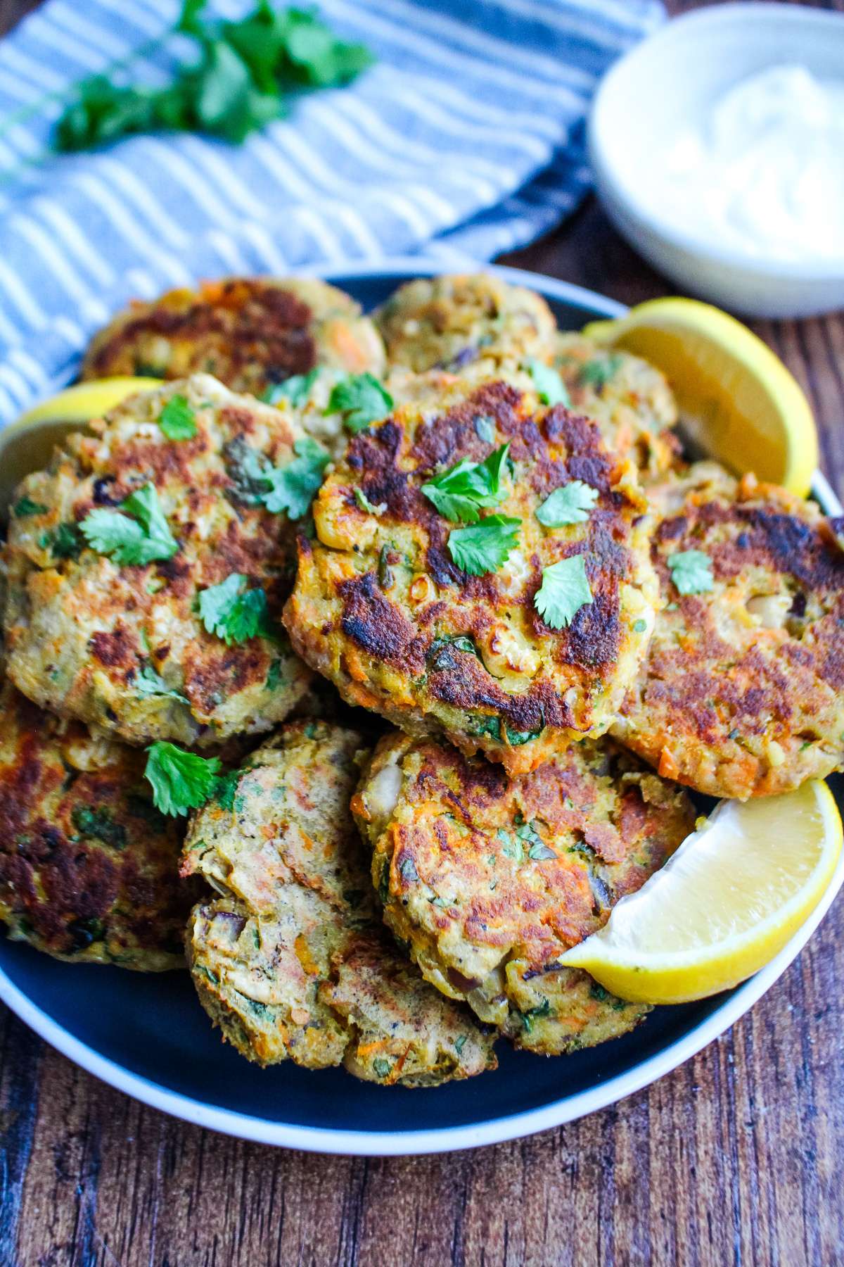 A closeup of sardine fish cakes on a plate with lemons and a sauce in a small bowl next to the plate.