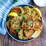 Sardine cakes served up on a plate with a blue napkin on the side and a small bowl of white sauce.