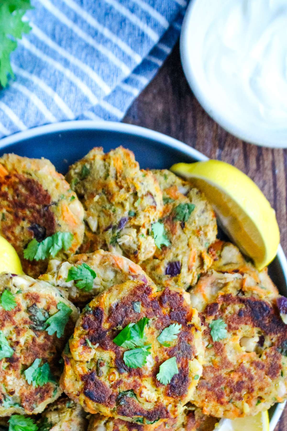 Sardine cakes with lemon wedge on a plate with a blue napkin next to the plate.