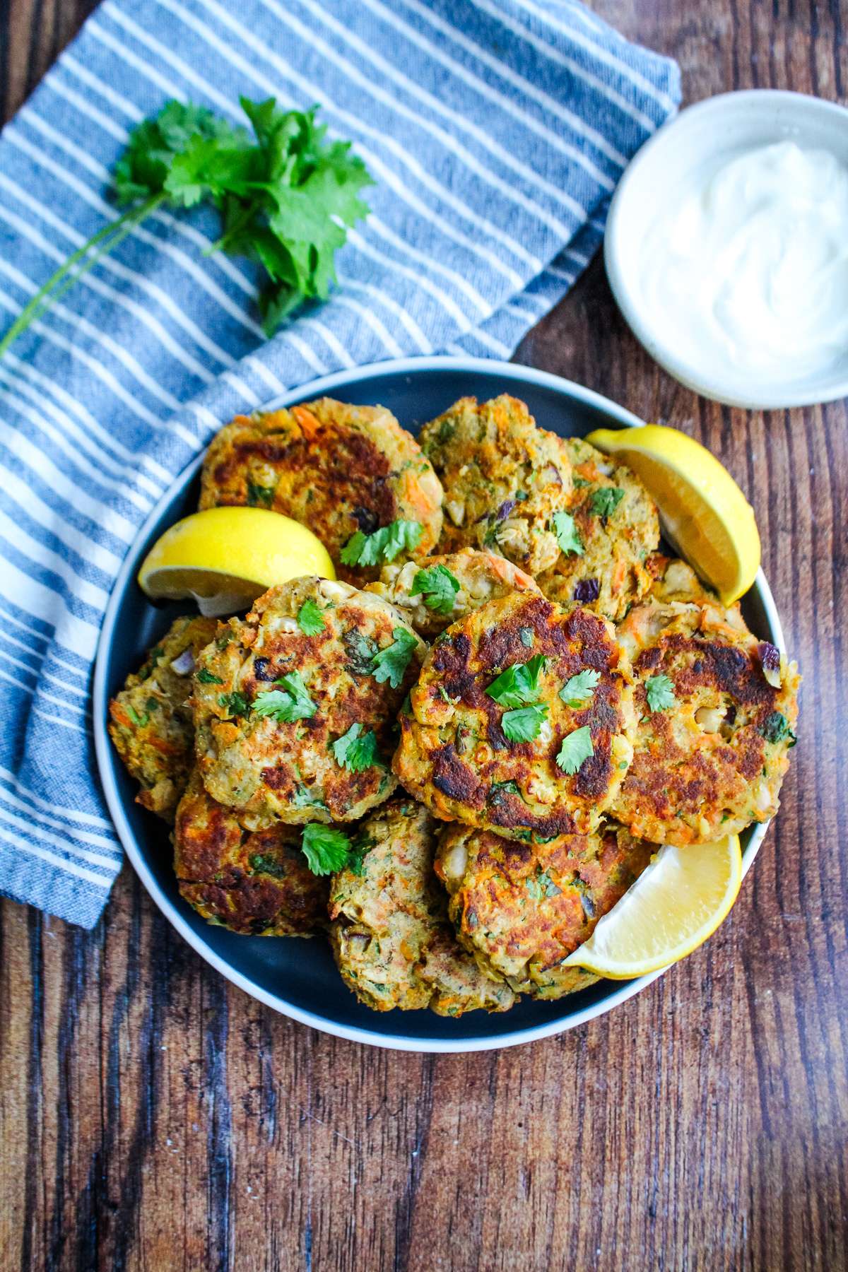  A plate full of sardine cakes on the table with lemons and a sauce.