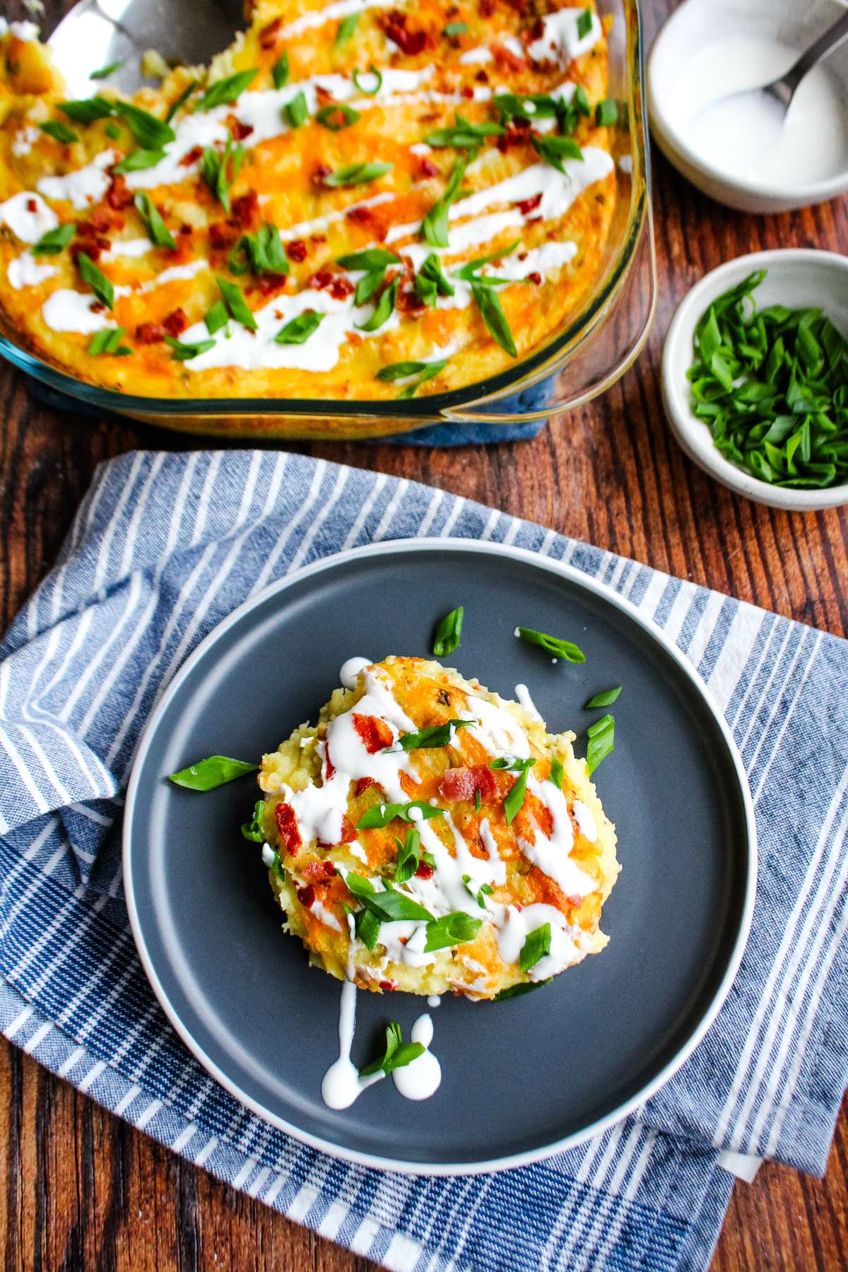 A serving of twice baked mashed potatoes on a plate with the casserole dish to the side.