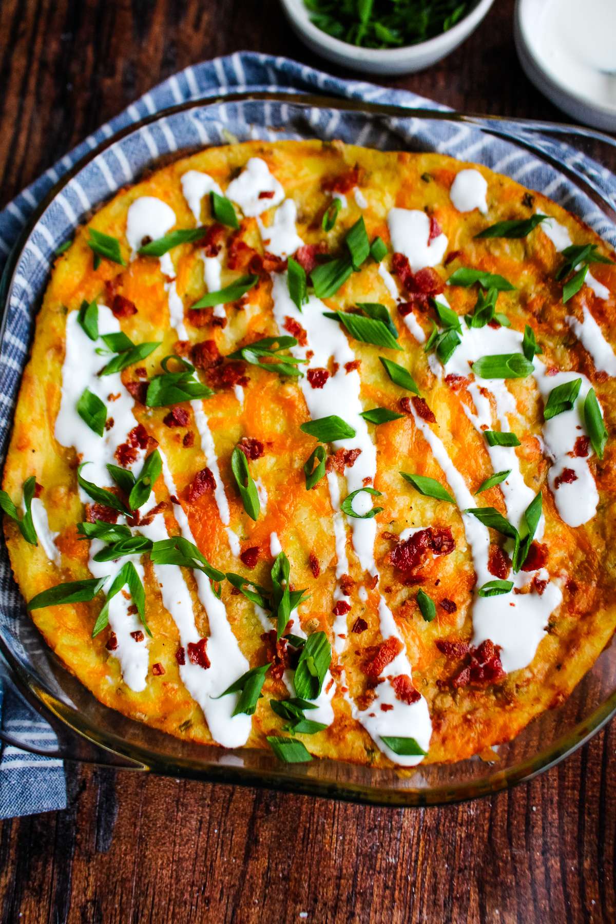 A casserole dish of twice baked mashed potatoes on the table in a dish and drizzled with sour cream.