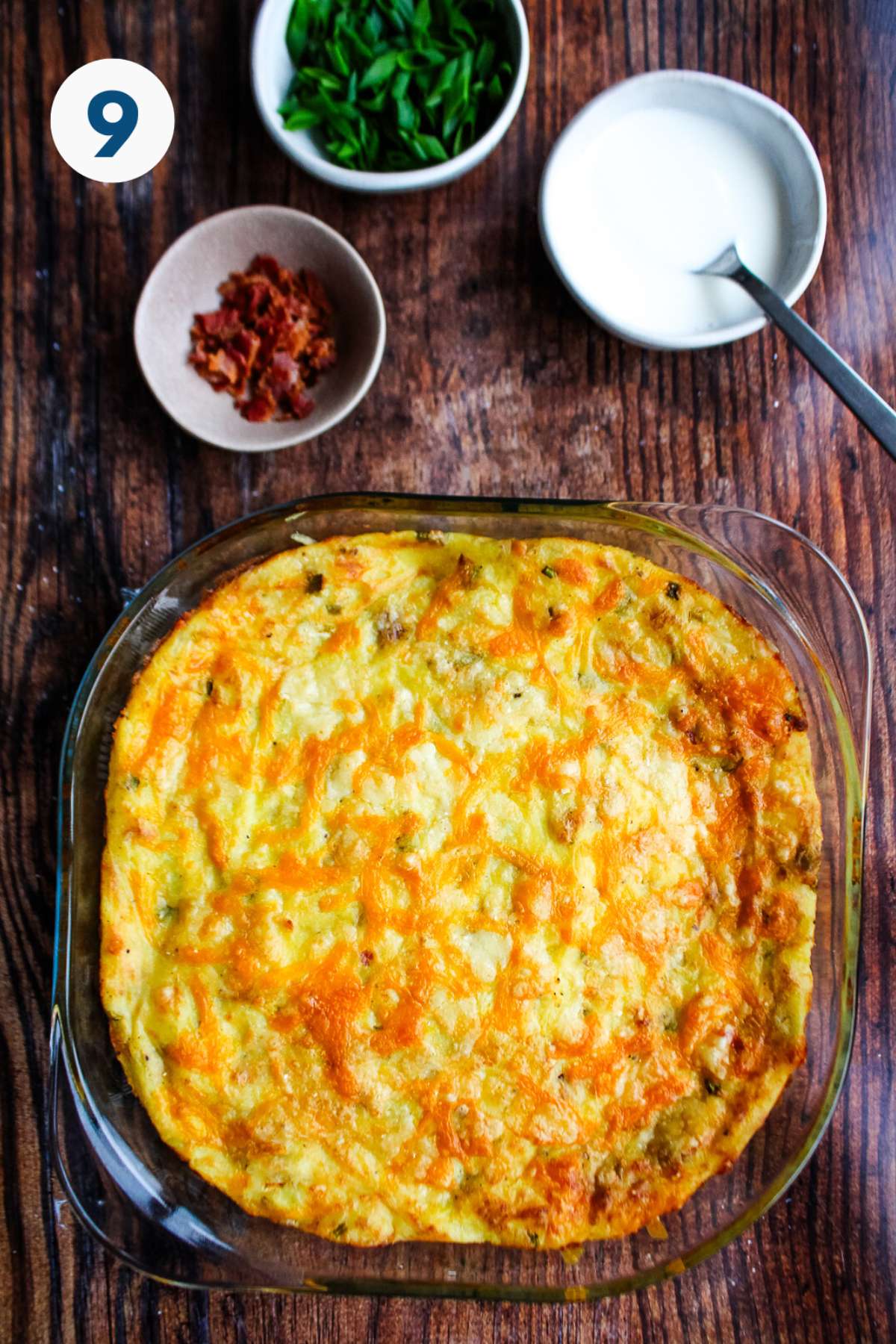 The mashed potato casserole on the table after baking with bacon, sour cream, and green onions in small bowls.