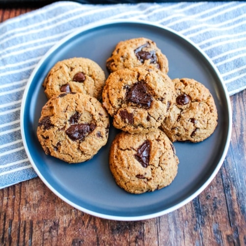 A plate of brown butter gluten free chocolate chip cookies on a blue plate with a blue striped towel underneath.