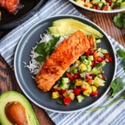 Salmon with pineapple salsa on a blue plate with avocado and rice.