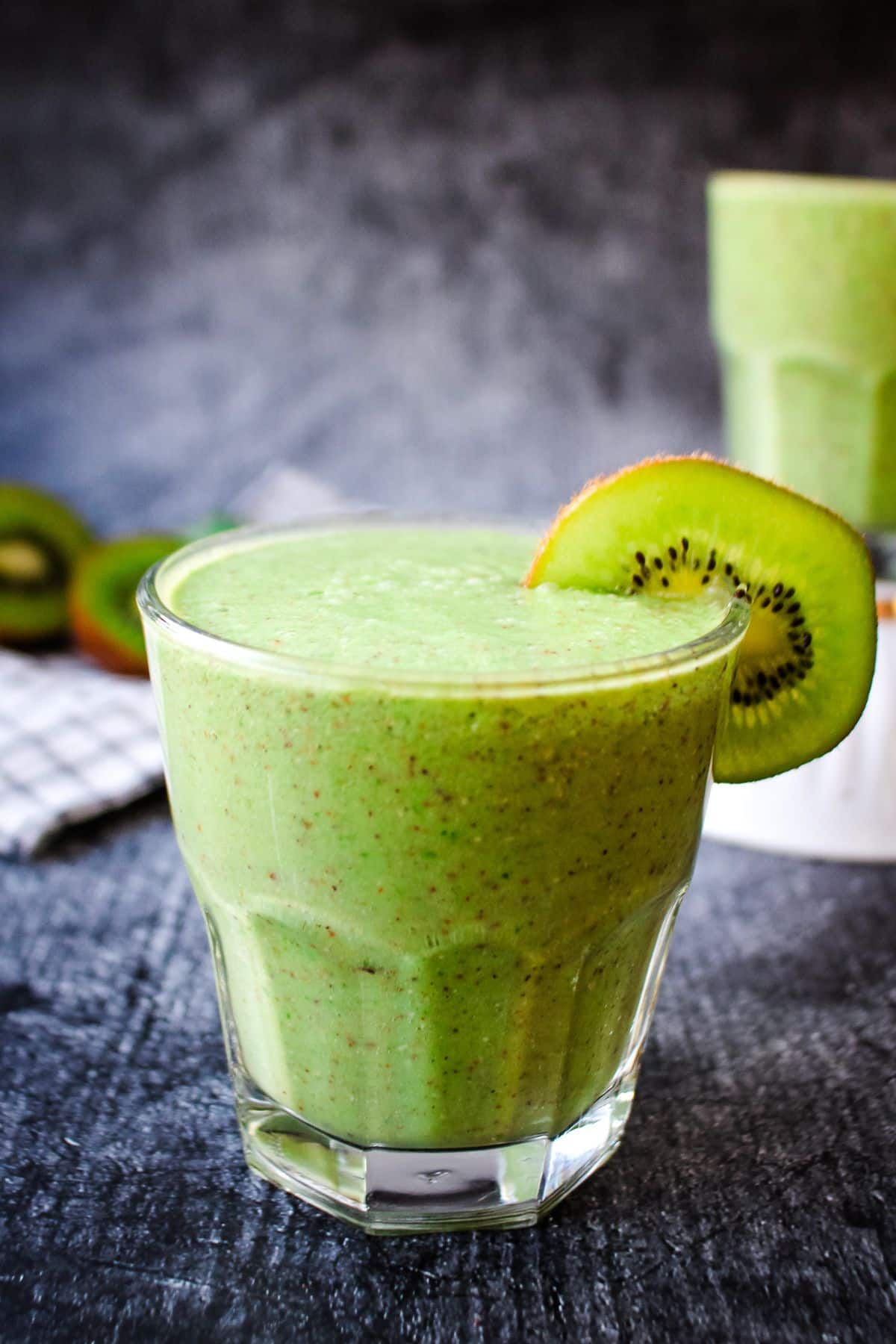 A green kiwi smoothie on the table with a kiwi on the glass rim.