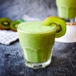 A kiwi smoothie for constipation on the table with kiwi in the background and another glass.