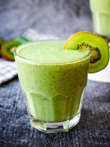 A kiwi smoothie for constipation on the table with kiwi in the background and another glass.
