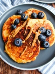 A plate of cottage cheese oatmeal pancakes with almond butter and blueberries.