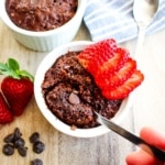 Chocolate protein mug cake on the table with a spoon dipping in to take a bite.