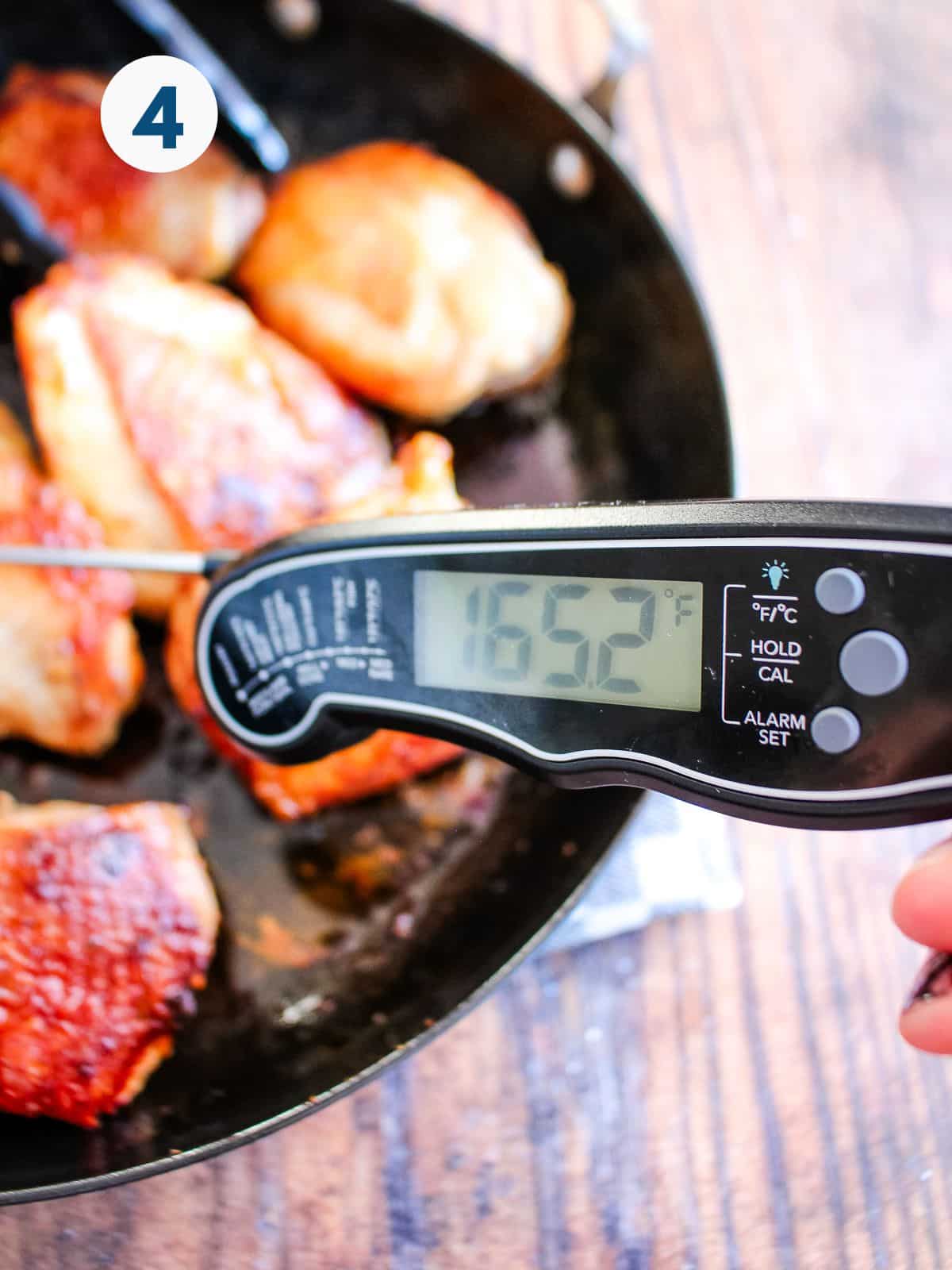 Tongs reaching into to grab a chicken thigh cooking in a cast iron skillet.