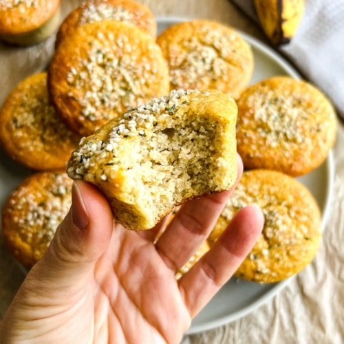 A hand holding up a almond flour banana muffin with a bite missing.