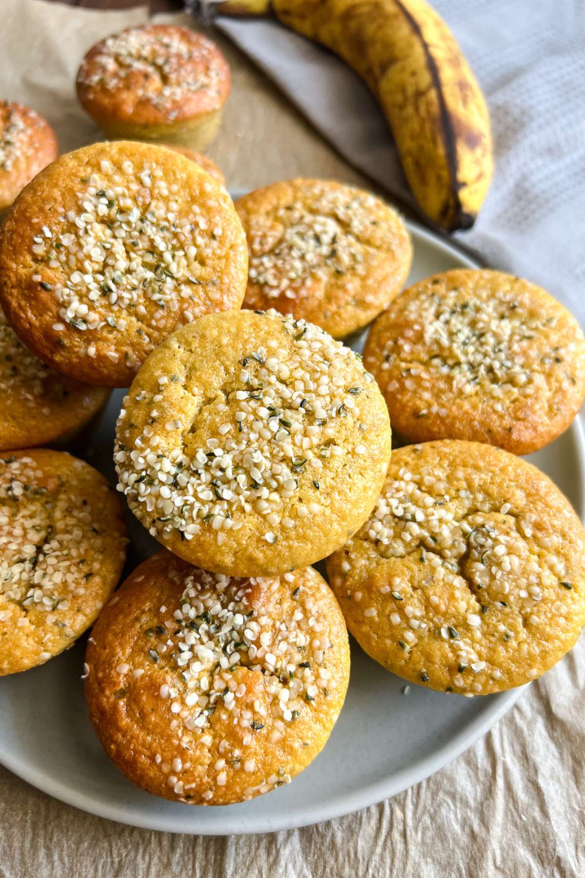 A plate of almond flour banana muffins topped with hemp seeds on the table with a banana in the background.