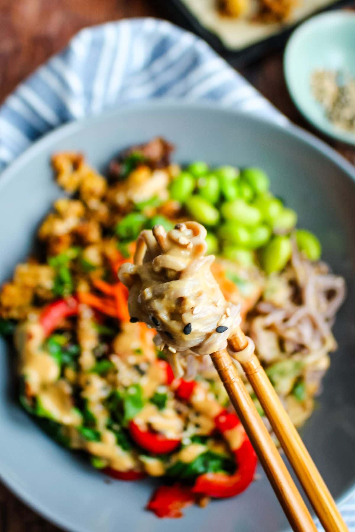 A pair of chopsticks holding a bite of soba noodles over the bowl.