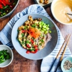 Sesame soba noodle bowl on the table with a bowl of sauce, garnishes, and chopsticks.
