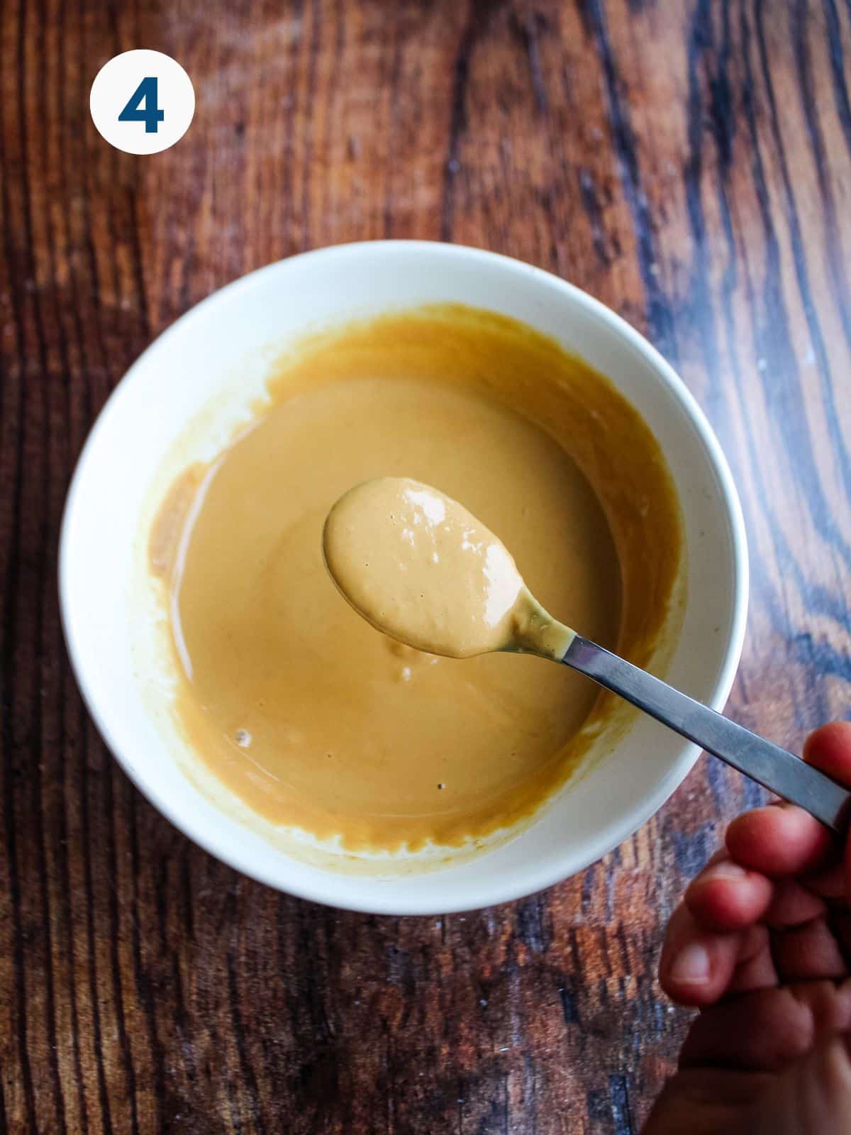 A bowl of miso tahini sauce with a spoon holding some above the bowl.