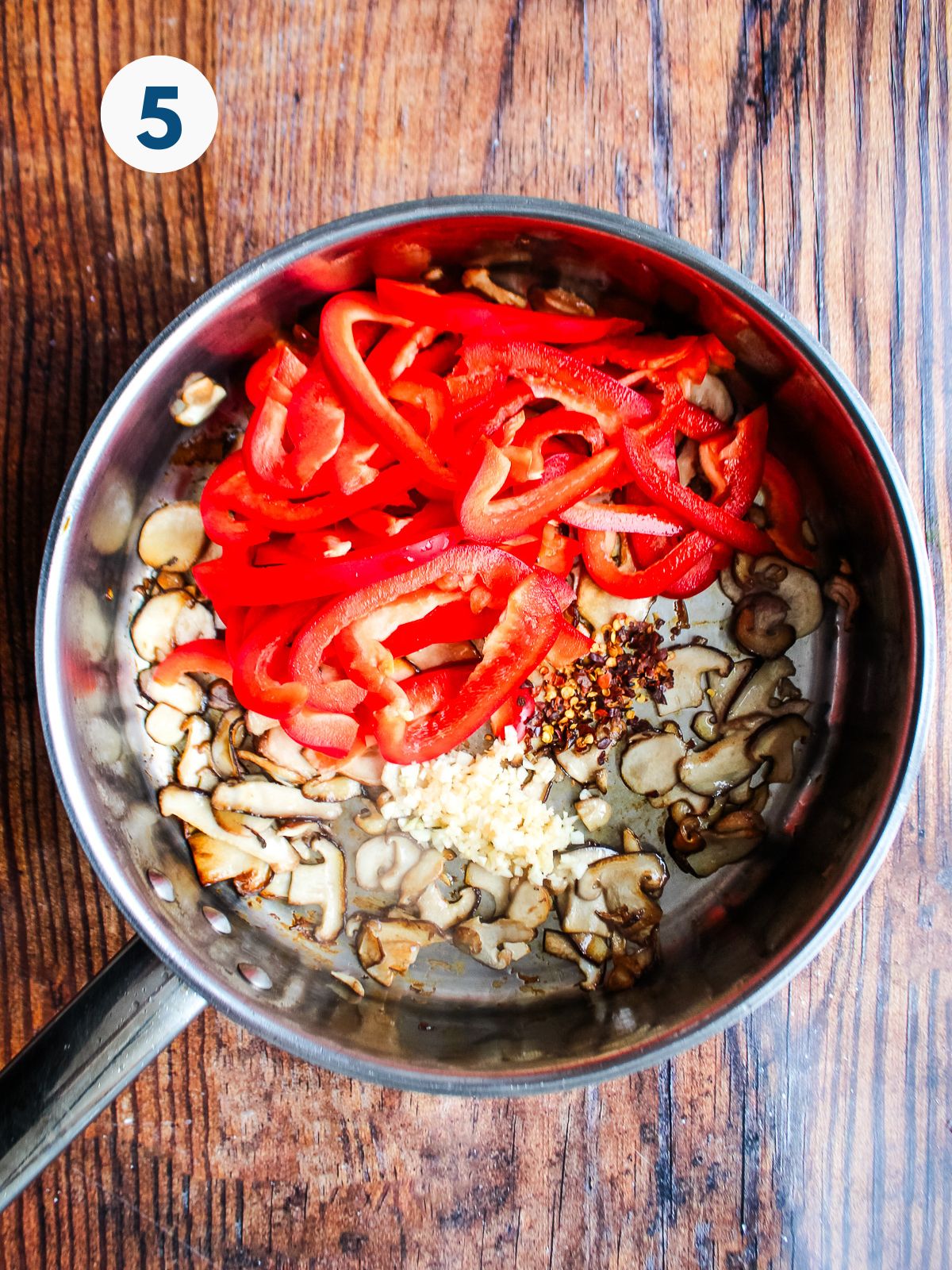Red peppers added to a skillet with sauteed onions.