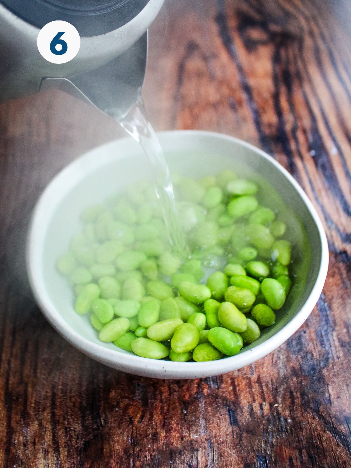 Edamame in a bowl with hot water poured over the top.