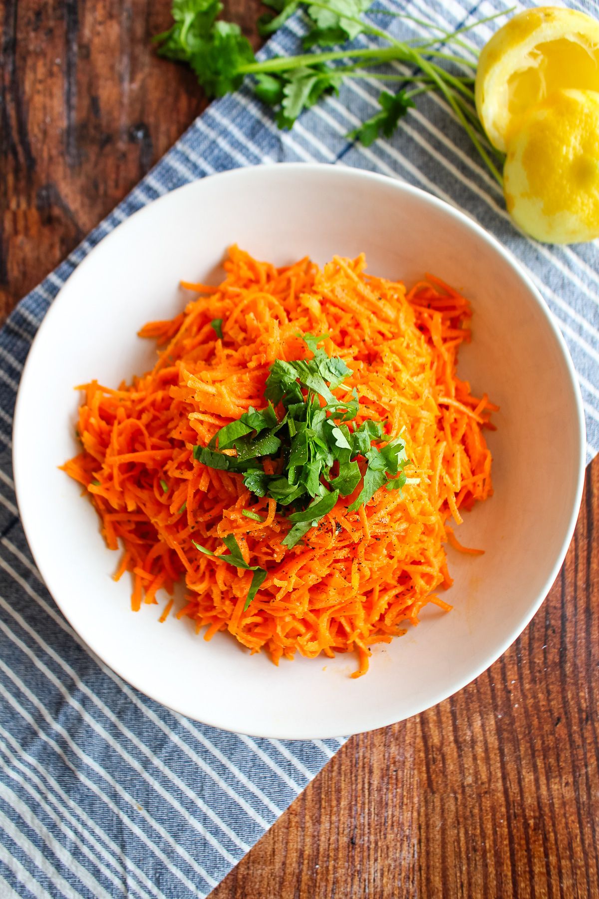 A bowl of Moroccan carrot salad on a table with blue and white tea underneath.